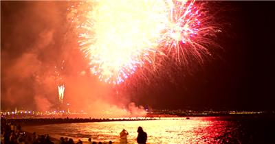 在晚上的庆祝活动中，人们欣赏在海边的天空中燃放的烟火。