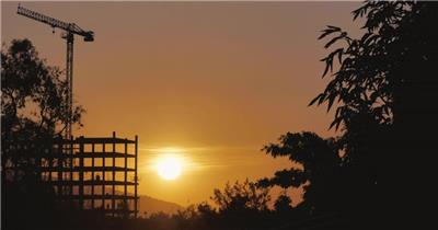 延时摄影日落夕阳下一座有塔式起重机和周围许多树木的建筑