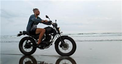 穿着牛仔夹克的男子在沙滩上骑摩托车