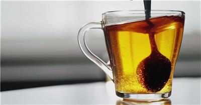 在透明玻璃茶杯中用勺子搅拌糖茶