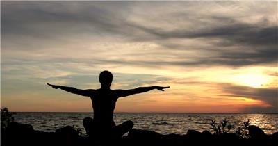 日落黄昏下男子坐在大海海边做瑜伽