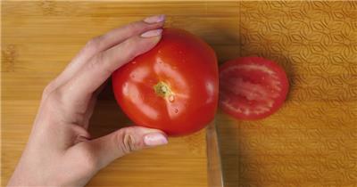 一个女人在板上将番茄切成厚片